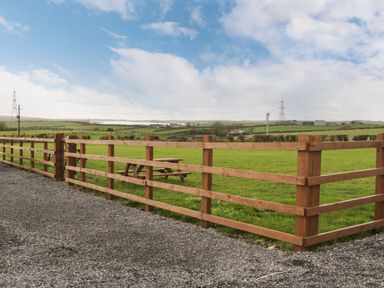 A gravel path with a wooden fence enclosing a green field and a picnic table at The Lodge in Rhosybol
