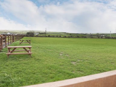 A grassy field with wooden picnic tables and a wooden fence in a rural area at The Lodge in Rhosybol