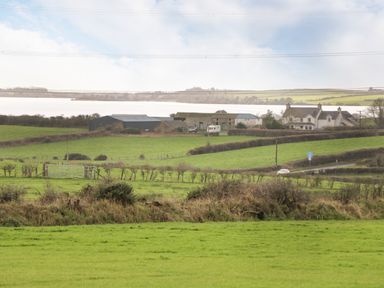 A rural landscape with green fields barns and a house near a body of water at The Lodge in Rhosybol