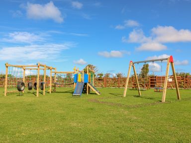 An outdoor playground with swings slides and climbing structures on grass at The Lodge in Rhosybol