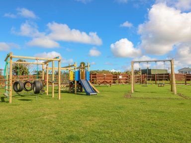 An outdoor playground with swings slides and climbing equipment on grass at The Lodge in Rhosybol