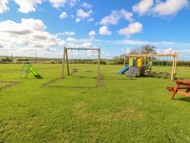 A children's playground with swings slides and climbing frames on a grass field at The Lodge in Rhosybol