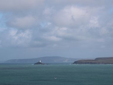 A seascape with a lighthouse on a rocky island and a coastline in the background at Tredarn in Connor Downs