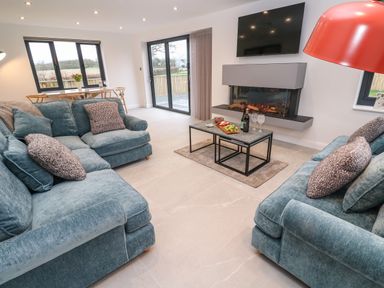 A living room with two blue sofas a coffee table with food and drinks a fireplace and a wall-mounted television at Tredarn in Connor Downs
