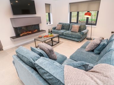 A living room with teal sofas a coffee table with snacks a fireplace and a wall mounted tv at Tredarn in Connor Downs