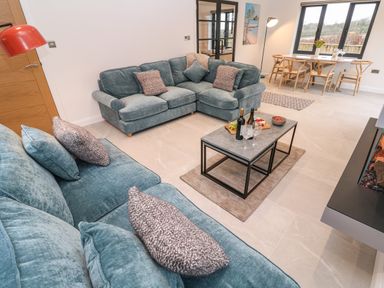 A living room with blue sofas a coffee table with wine and glasses and a dining table by a window at Tredarn in Connor Downs
