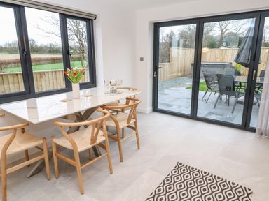 A dining area with a white table and wooden chairs next to windows and glass doors leading to a patio at Tredarn in Connor Downs