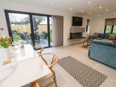 A living room with a blue sofa a wall mounted television a patterned rug and a dining table near glass doors at Tredarn in Connor Downs