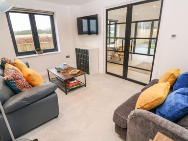 A living room with two sofas cushions a coffee table and a mounted TV next to glass doors leading to a dining area at Tredarn in Connor Downs