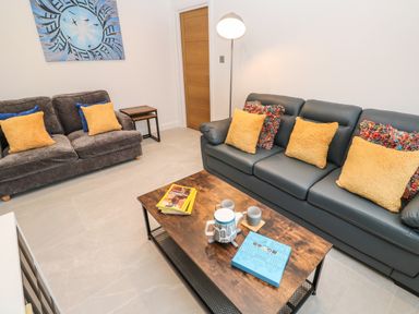 A living room with two sofas a wooden coffee table with books and teapot and wall art at Tredarn in Connor Downs