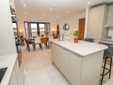 A kitchen with an island countertop and dining table with chairs near windows at Tredarn in Connor Downs