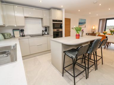 A kitchen with an island and bar stools and modern cabinets at Tredarn in Connor Downs