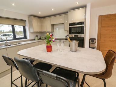A kitchen with an island countertop with chairs a vase of flowers and a bucket with a bottle of champagne at Tredarn in Connor Downs