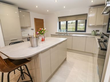 A kitchen with beige cabinets a countertop island with flowers an ice bucket and champagne at Tredarn in Connor Downs