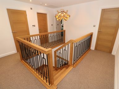 A hallway with carpeted floor wooden doors and wooden and metal staircase railing at Tredarn in Connor Downs