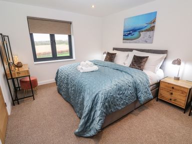 A bedroom with a bed covered with a blue comforter bedside tables a window and a small desk at Tredarn in Connor Downs