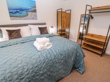 A bedroom with a bed with pillows and folded towels and wooden shelves with a mirror at Tredarn in Connor Downs