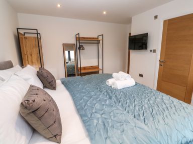 A bedroom with a bed a wall-mounted tv a wooden door and a mirror at Tredarn in Connor Downs