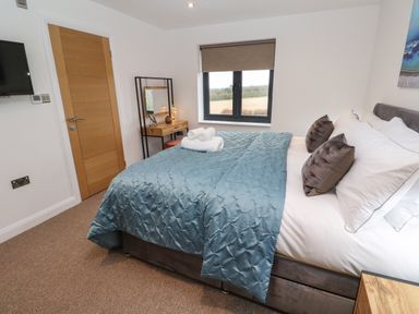 A bedroom with a bed covered by a blue blanket and two rolled towels on top at Tredarn in Connor Downs