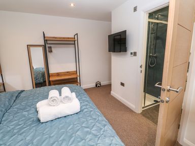 A bedroom with a bed and rolled towels on it a standing mirror a wooden shelf a wall-mounted TV and an open door leading to a shower at Tredarn in Connor Downs