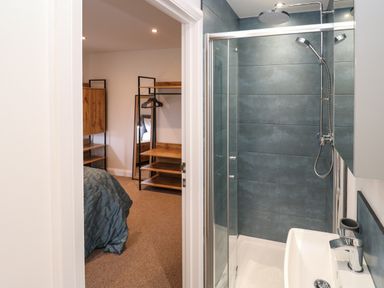 A bathroom with a shower and a sink next to a bedroom with a bed and wooden shelves at Tredarn in Connor Downs