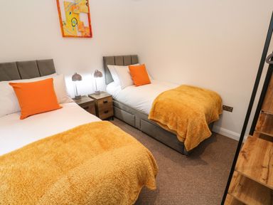 A bedroom with two single beds orange pillows and throws and a wooden nightstand with two lamps at Tredarn Connor Downs