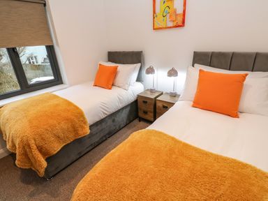 A bedroom with two single beds orange pillows and blankets bedside tables with lamps at Tredarn in Connor Downs