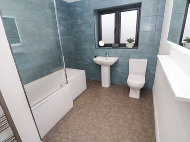 A bathroom with a bathtub shower glass and a toilet with a sink below a window at Tredarn in Connor Downs