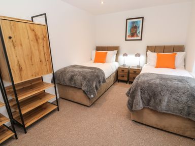 A bedroom with two single beds gray blankets orange pillows a wooden cabinet and side tables with lamps at Tredarn in Connor Downs