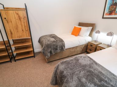 A bedroom with two single beds a wooden cabinet with shelves and bedside tables with lamps at Tredarn in Connor Downs