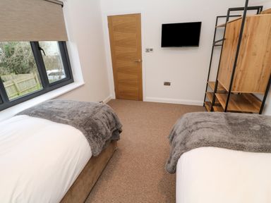 A bedroom with two beds a wooden door a wall-mounted television and a wooden shelving unit at Tredarn in Connor Downs