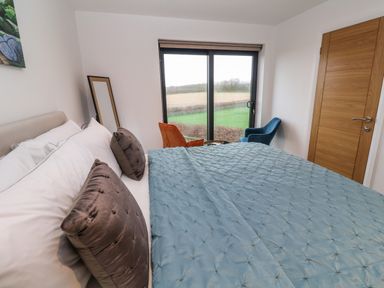 A bedroom with a bed blue quilt orange and blue chairs near window and wooden door at Tredarn in Connor Downs