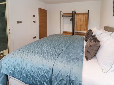 A bedroom with a blue quilted bedspread, brown pillows, wooden door, and wooden shelving at Tredarn in Connor Downs