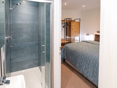 A shower area with blue tiles next to a bedroom with a blue bedspread and wooden wardrobe at Tredarn in Connor Downs