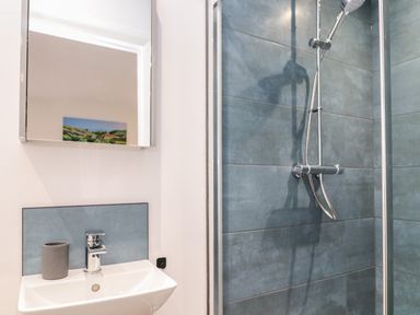 A bathroom with a sink faucet and a gray cup next to a mirror and a shower with gray tiled walls at Tredarn in Connor Downs