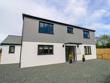 A modern two-story house with grey cladding on the upper floor white walls on the lower floor black framed windows and a gravel front yard at Tredarn in Connor Downs