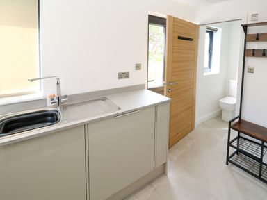 A kitchen area with a sink and countertop next to a wooden door and a toilet visible through an open doorway at Tredarn in Connor Downs