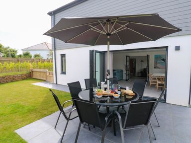 An outdoor patio with a round table, six chairs, an umbrella, and snacks in a garden at Tredarn in Connor Downs