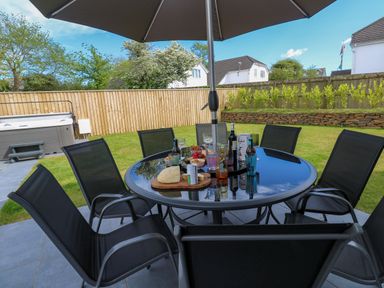 A garden patio with a glass table set for drinks and snacks under an umbrella with chairs around at Tredarn in Connor Downs