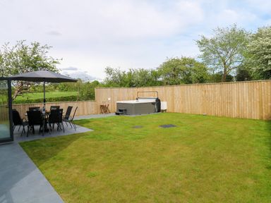 A backyard with a dining table under an umbrella a hot tub and wooden fencing at Tredarn in Connor Downs