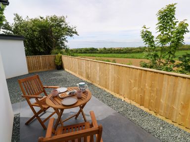 An outdoor patio area with wooden table and two chairs with cups plates and snacks with a wooden fence and green fields in the background at Tredarn in Connor Downs