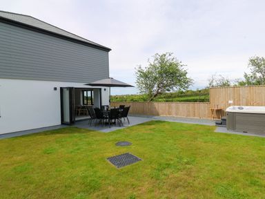 A garden with a patio table and chairs under an umbrella next to a hot tub and a fenced yard at Tredarn in Connor Downs