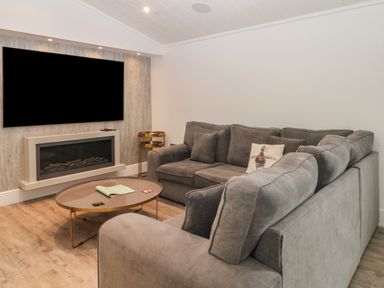 A living room with a gray sectional sofa a round coffee table a wall-mounted television and a fireplace at Ruperts Retreat in Nateby near Garstang