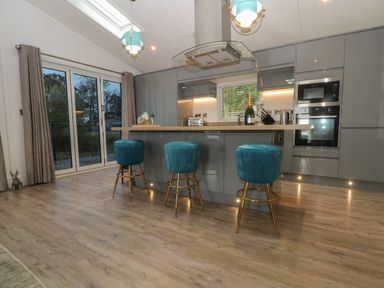 A kitchen with a central island with three teal stools and grey cabinets at Ruperts Retreat in Nateby near Garstang