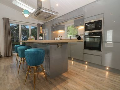 A kitchen with grey cabinets a wooden countertop blue bar stools and a sliding glass door at Ruperts Retreat in Nateby near Garstang