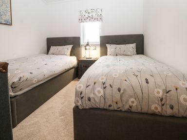 A bedroom with two single beds a small table lamp on a nightstand under a window at Ruperts Retreat in Nateby near Garstang