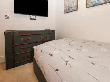 A bedroom corner with a bed covered in floral patterned bedding a vintage style dresser and a wall mounted television at Ruperts Retreat in Nateby near Garstang