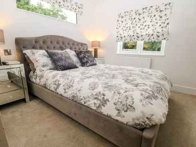 A bedroom with a bed featuring floral bedding and two pillows bedside tables with lamps and windows with floral blinds at Ruperts Retreat in Nateby near Garstang