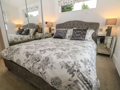 A bedroom with a large bed with floral bedding two bedside tables with lamps and mirrored wardrobes at Ruperts Retreat in Nateby near Garstang