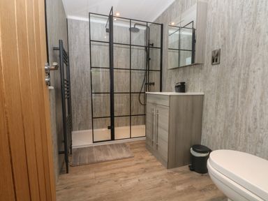 A bathroom with a shower enclosure with black frame a vanity with sink a mirror a toilet and a wooden floor at Ruperts Retreat in Nateby near Garstang